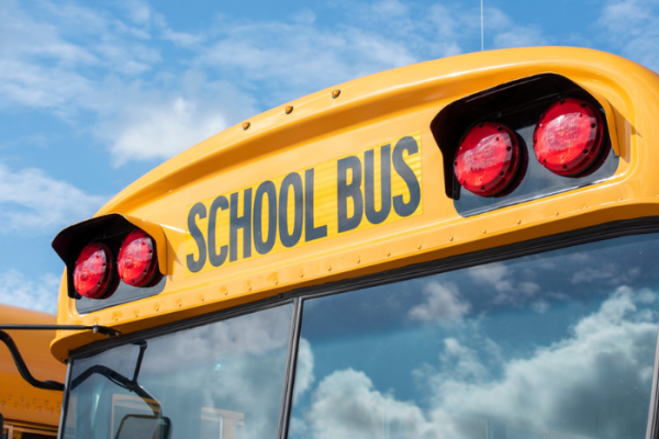 Closeup of front of yellow school bus with white clouds and blue sky reflected in windshield.