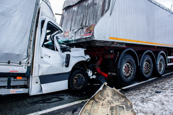 Severe truck accident showing white delivery vehicle crushed under trailer