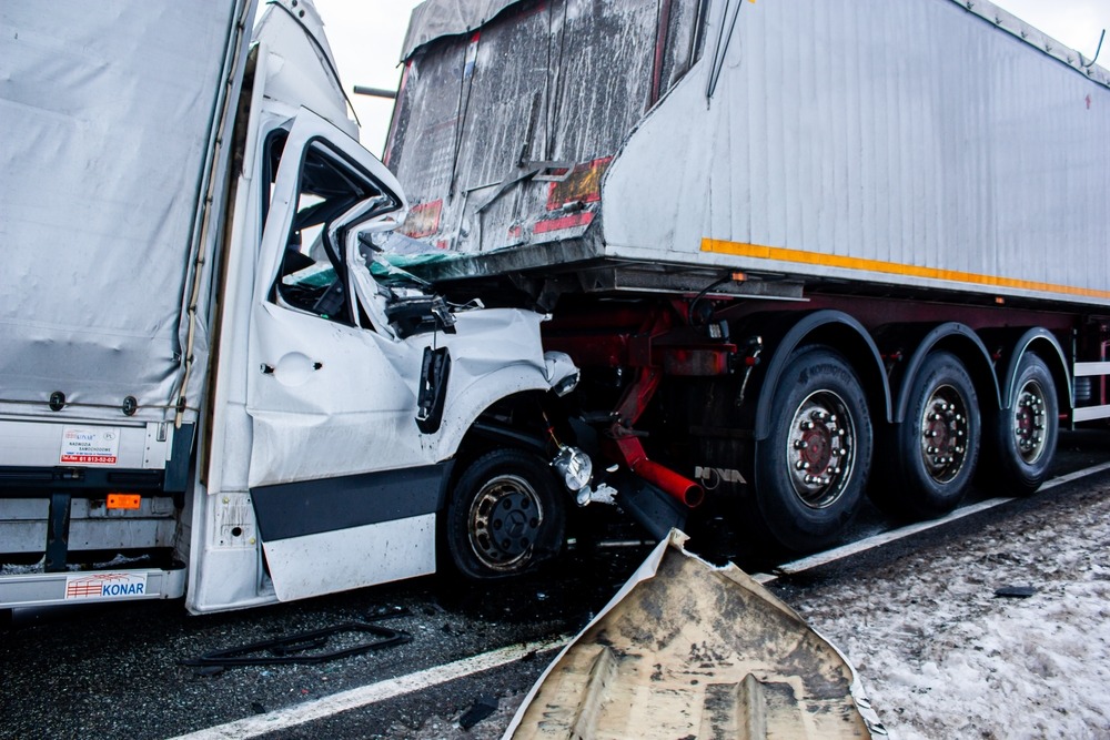 Severe truck accident showing white delivery vehicle crushed under trailer