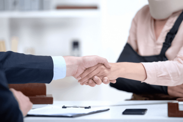 An attorney and an injured client review a trucking accident settlement agreement in a law office with a blurred semi-truck visible through the window.