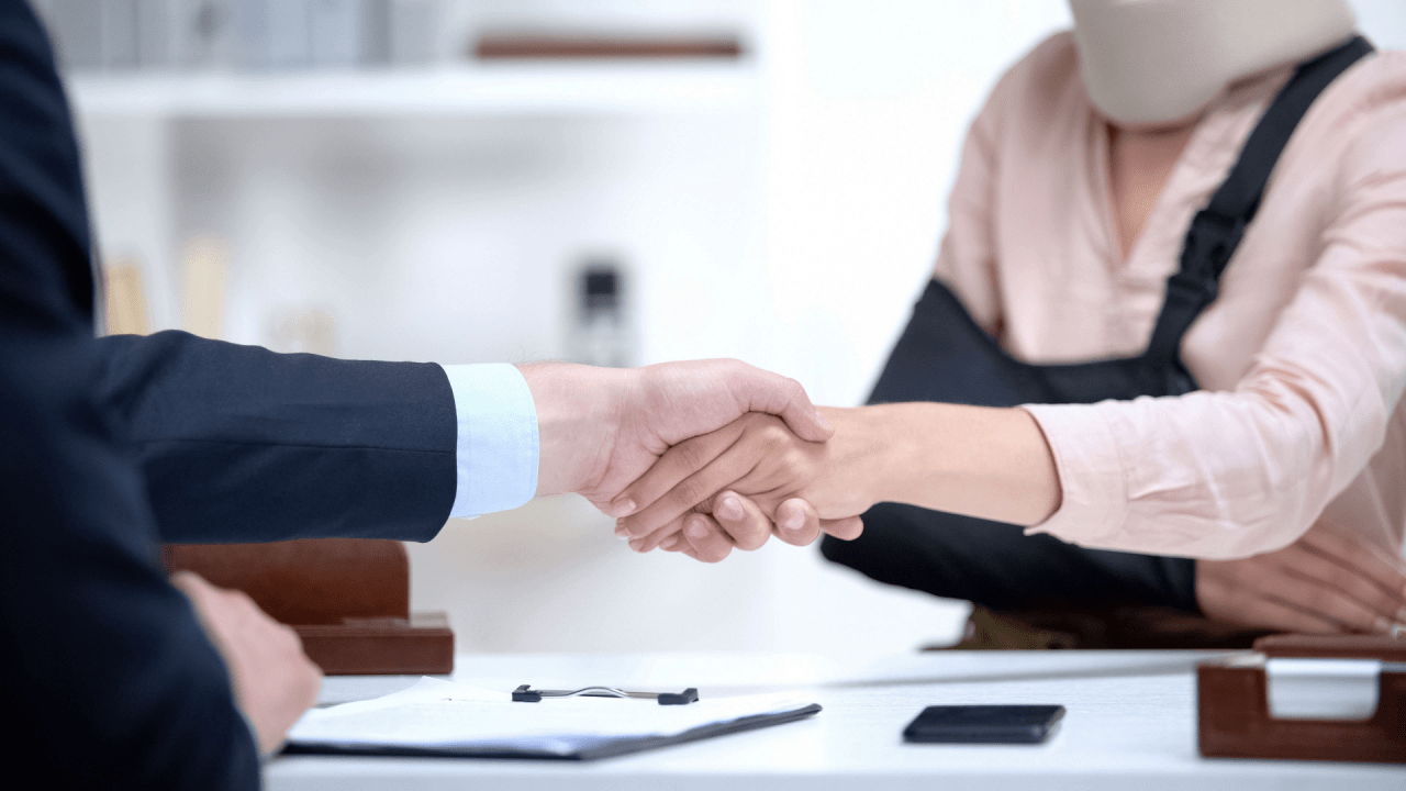 An attorney and an injured client review a trucking accident settlement agreement in a law office with a blurred semi-truck visible through the window.