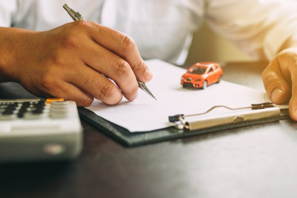 Person reviewing vehicle accident paperwork with toy car on clipboard and calculator nearby