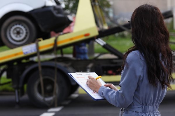Insurance adjuster assessing damaged vehicle being towed after an accident