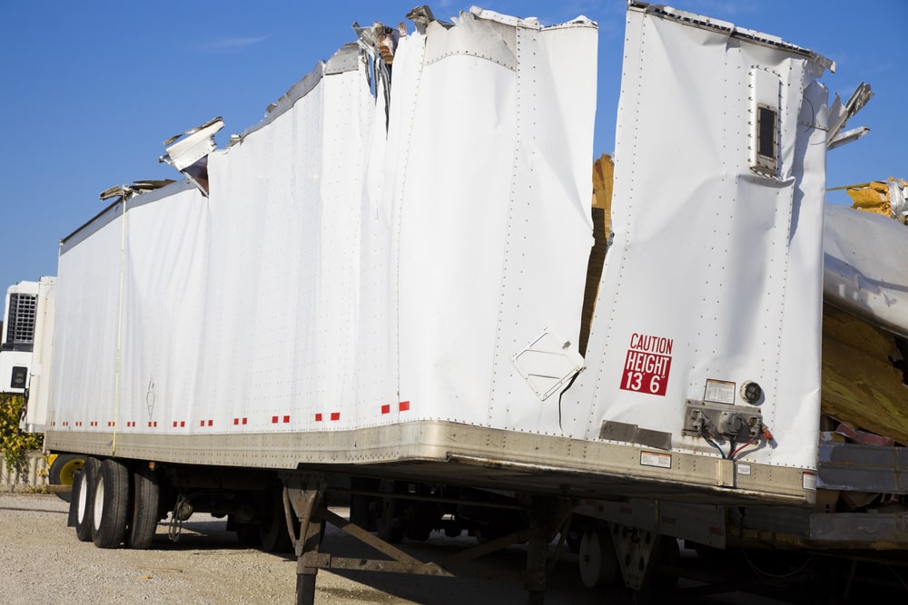 Severely damaged white semi-truck trailer with roof torn open
