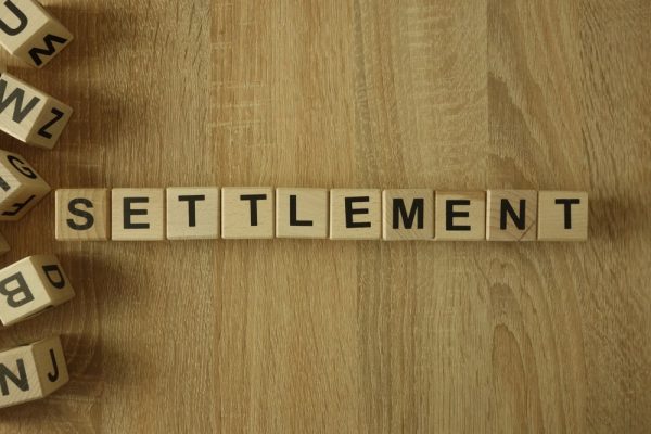 The word "Settlement" is spelled out using wooden letter blocks on a light wood surface