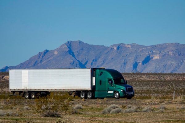 A green 18-wheeler truck driving through a California desert highway