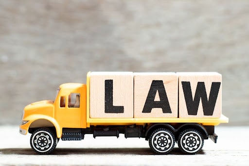 Yellow toy truck carrying wooden blocks spelling “LAW” – symbolizing truck accident legal services