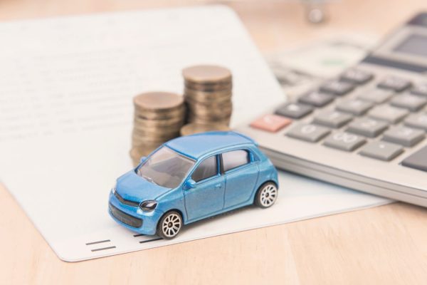 Miniature blue car with stacked coins and calculator representing car accident settlement and legal fees