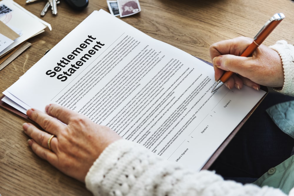 Person signing a printed settlement statement at a desk