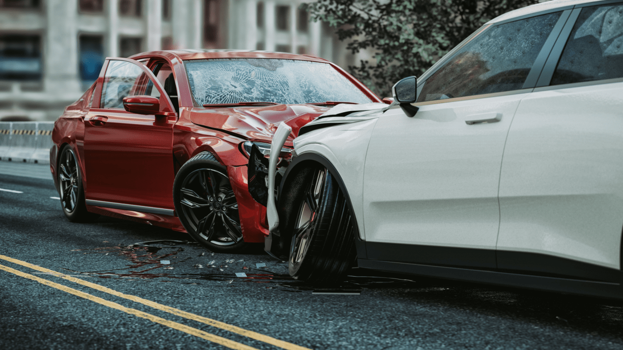 Two damaged cars after a collision on a city street - a red sedan with front-end damage and cracked windshield, and a white SUV with side damage, with debris scattered on the road