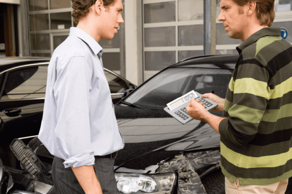 Two men discussing a car transaction with a calculator and paperwork in front of a black vehicle