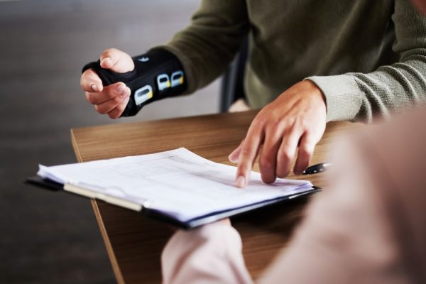 Injured person reviewing legal documents with a brace on their hand, discussing liability with a professional.