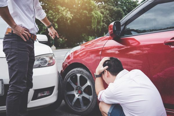 Man pointing at red car after collision, other man crouching in distress—depicting a scene of vehicle negligence.