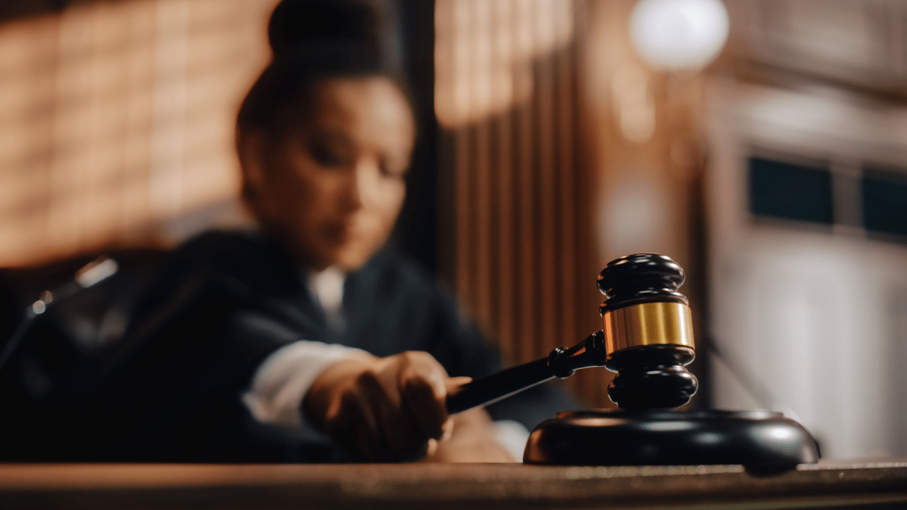 Close-up of judge's gavel with brass band in foreground while robed judge works at bench in blurred background