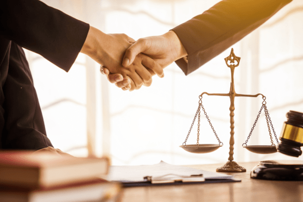Legal professionals shaking hands over scales of justice representing how settlement amounts are determined in personal injury cases