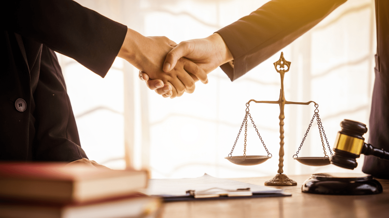 Legal professionals shaking hands over scales of justice representing how settlement amounts are determined in personal injury cases