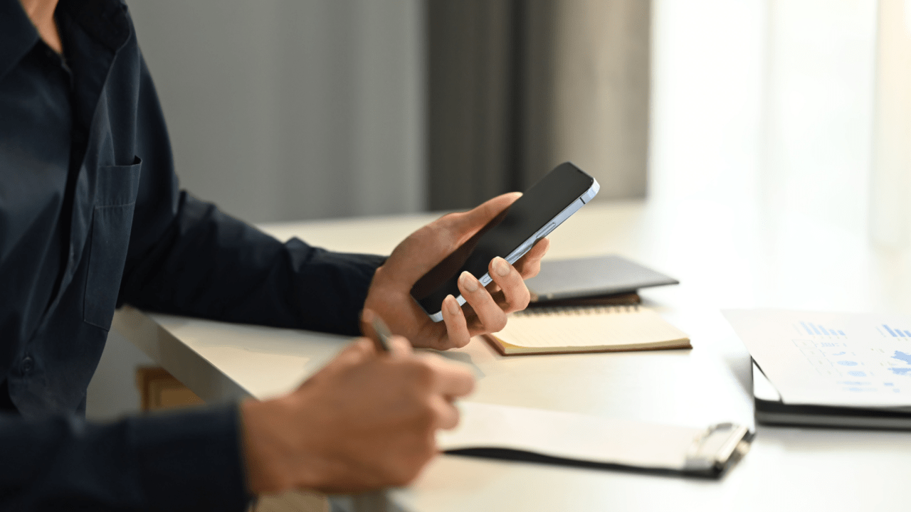 Professional using smartphone to research how does insurance affect settlements while reviewing legal documents at desk