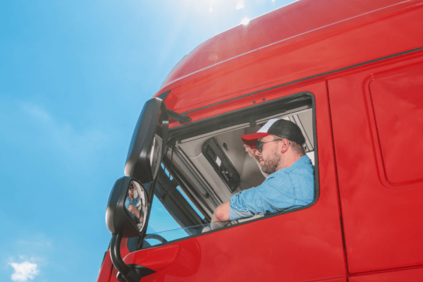 Professional truck driver in red semi-truck cab learning about truck driver laws and pay