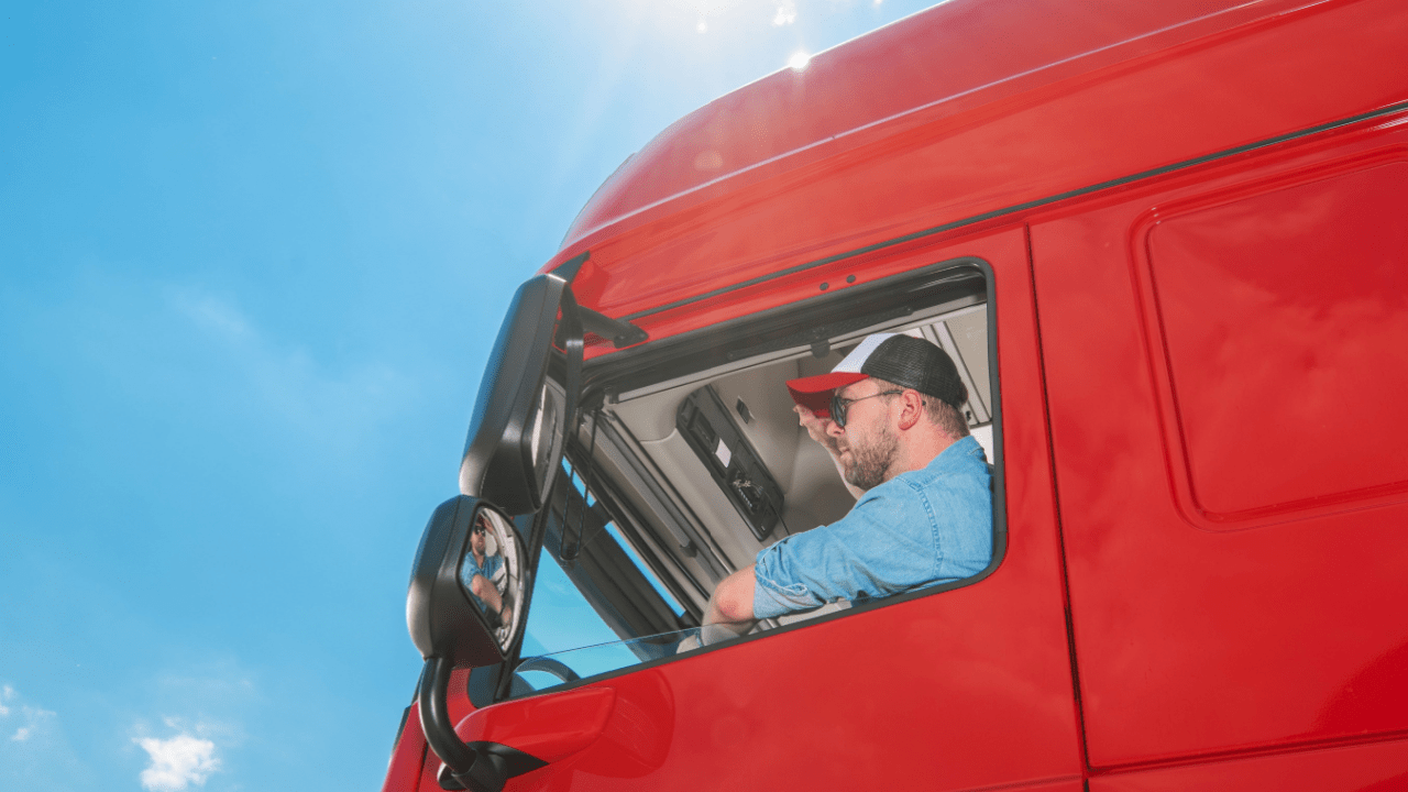 Professional truck driver in red semi-truck cab learning about truck driver laws and pay