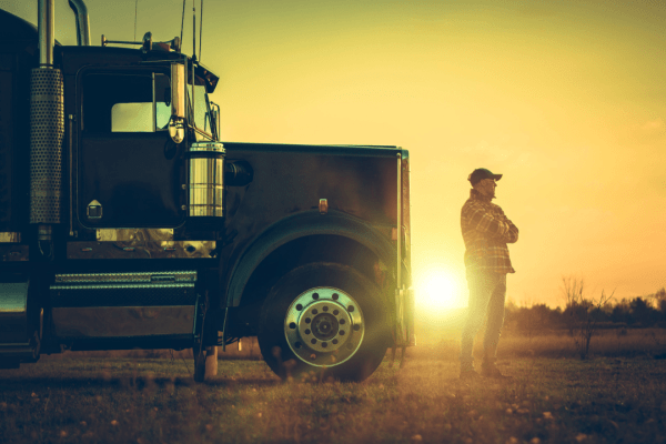 Truck driver at sunset beside semi-truck contemplating trucking violations and DOT penalties