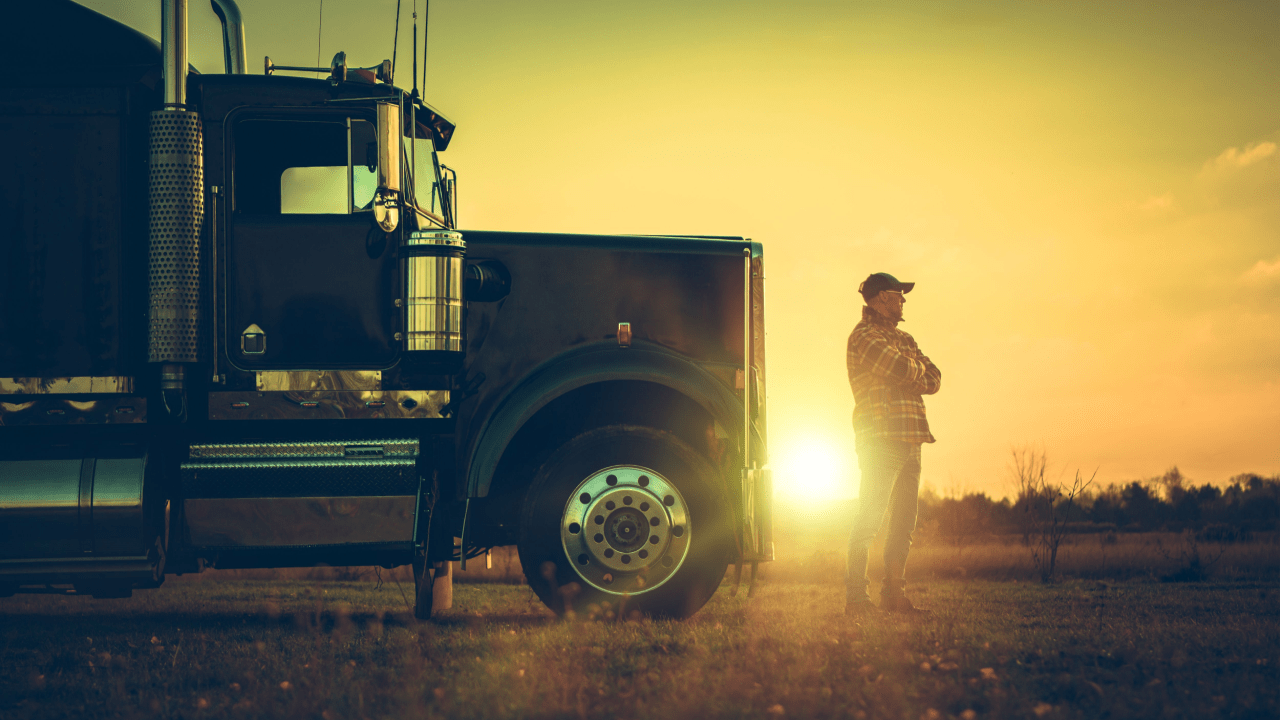 Truck driver at sunset beside semi-truck contemplating trucking violations and DOT penalties