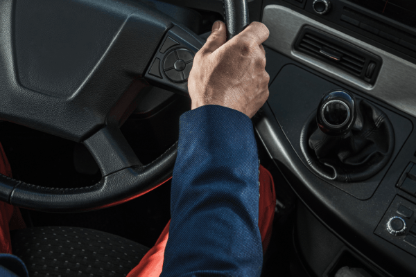 Truck driver hand on steering wheel in commercial cab learning what is a CMV violation