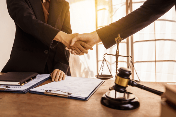 Two attorneys shaking hands over legal documents discussing what is a reasonable settlement offer with scales of justice and gavel on desk