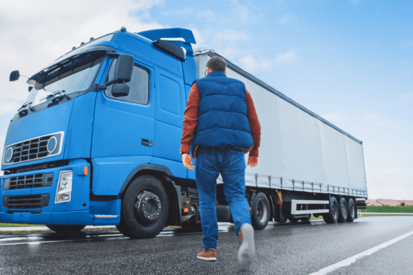 Commercial truck driver walking toward blue semi-truck illustrating what is the split sleeper rule rest period violations