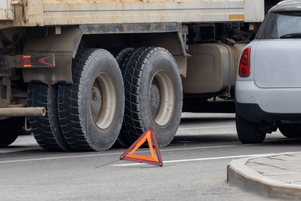 Truck accident scene with emergency warning triangle showing collision between commercial vehicle and passenger car requiring settlement negotiation timeline