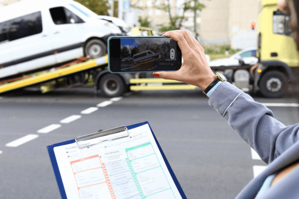 What makes a truck accident settlement higher or lower - Person documenting accident scene with smartphone and insurance claim form after commercial vehicle collision