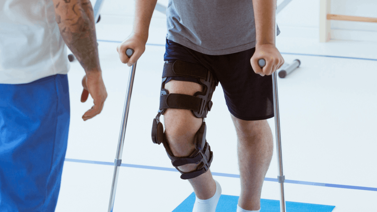 Physical therapy after accident — patient using crutches with knee brace during rehabilitation session