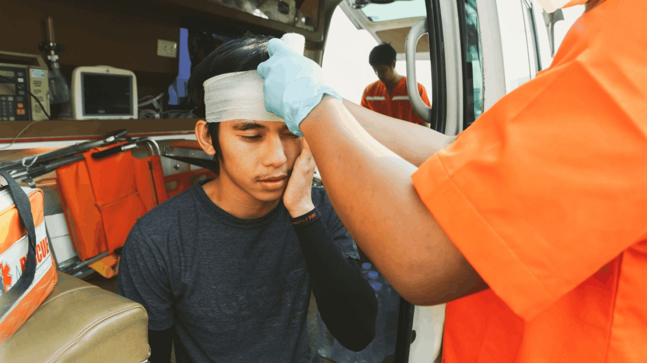 Paramedic providing truck accident medical treatment to an injured man with a head bandage inside an ambulance