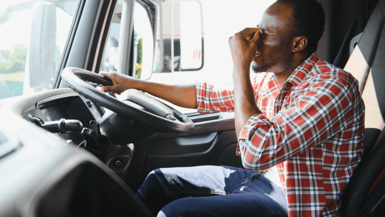 Drowsy truck driver rubbing eyes at wheel
